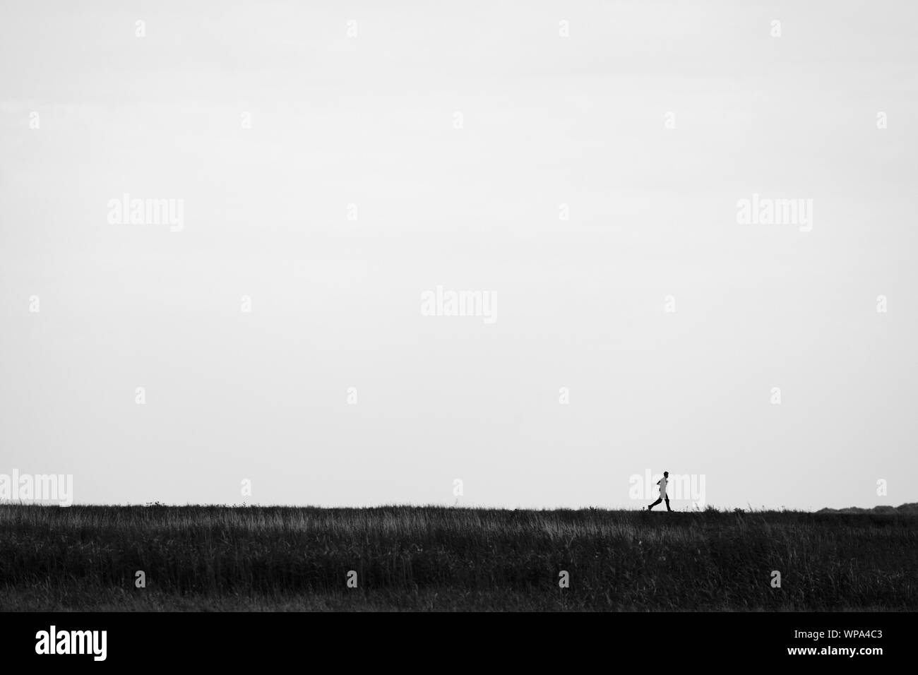 Giovane uomo che corre sulla parte superiore di una banca nelle paludi del North Norfolk. Foto Stock