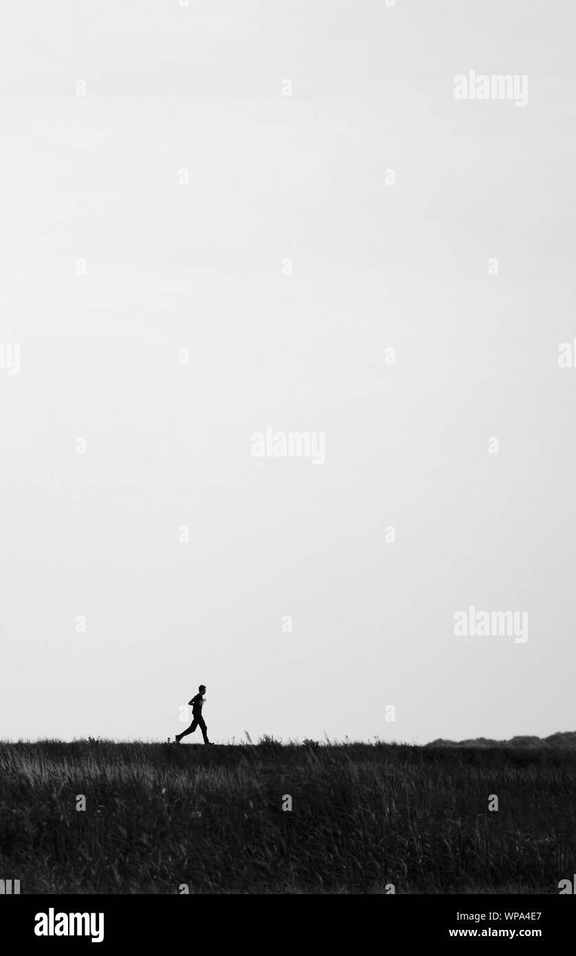 Giovane uomo che corre sulla parte superiore di una banca nelle paludi del North Norfolk. Foto Stock