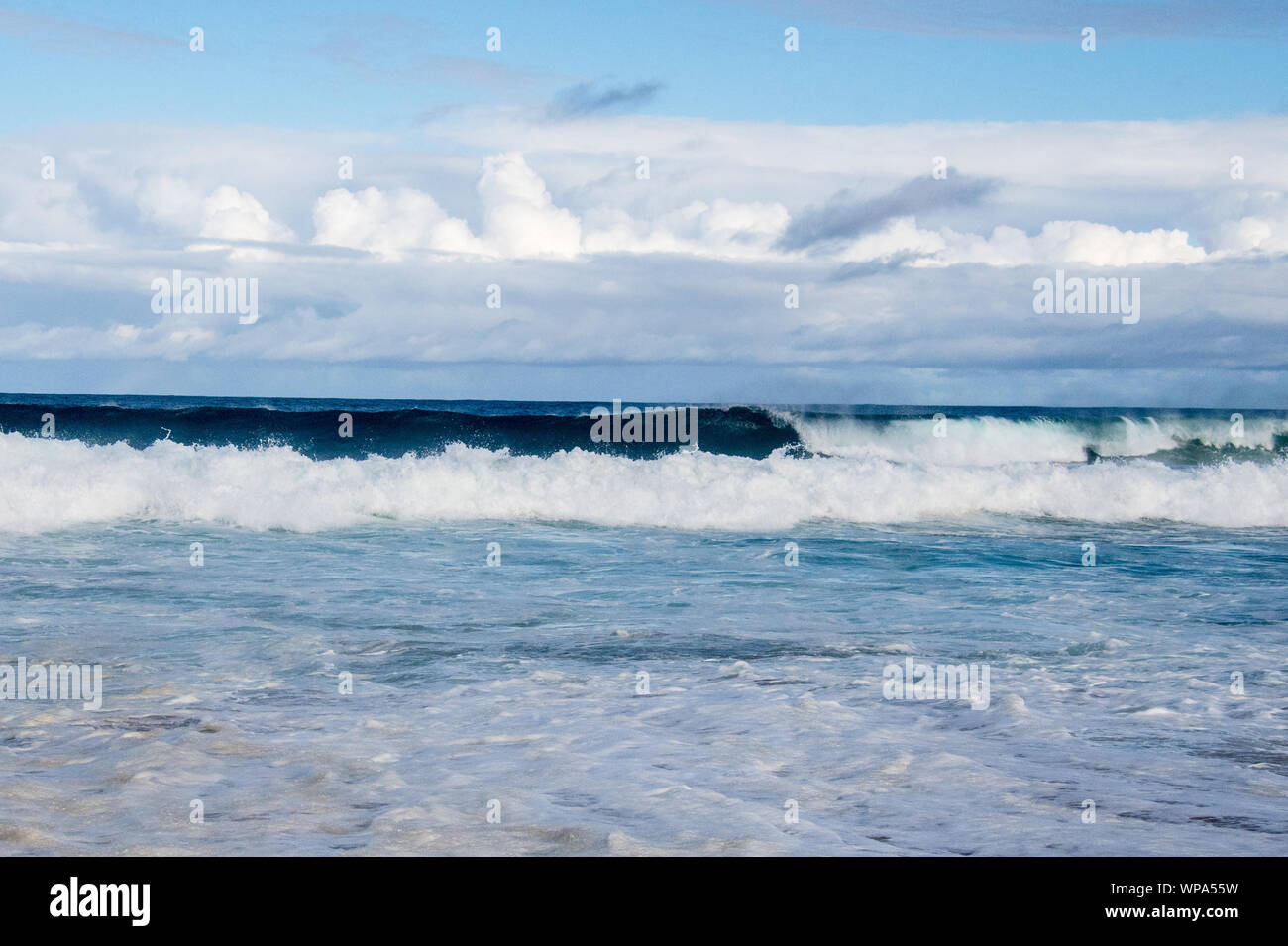 Serena seascape con acque blu e nuvole drammatico e fredde acque portando la marea sulla costa. Ci sono belle onde che si infrangono Foto Stock