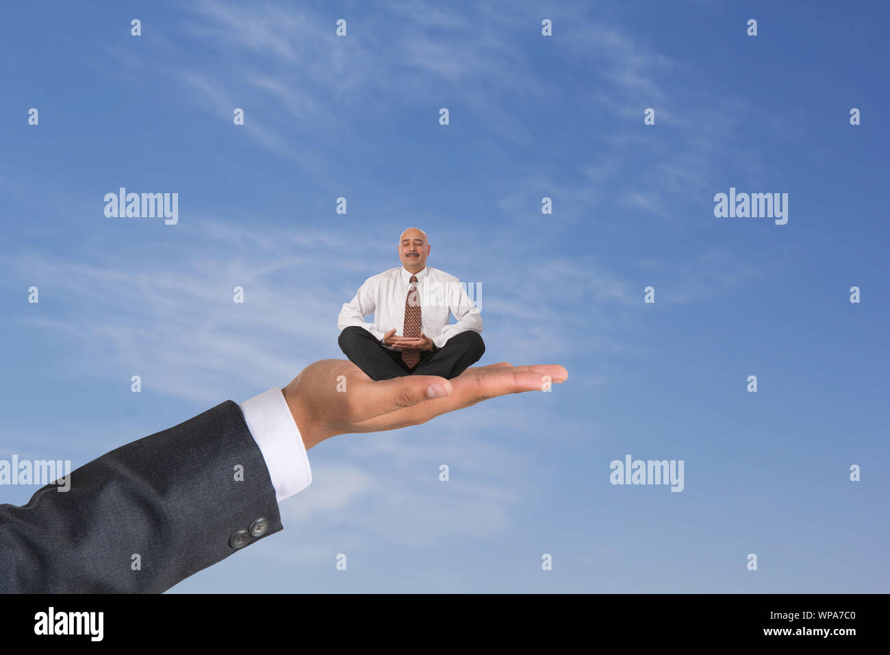 Uomo d'affari seduto su una mano umana e che fa yoga posa Foto Stock