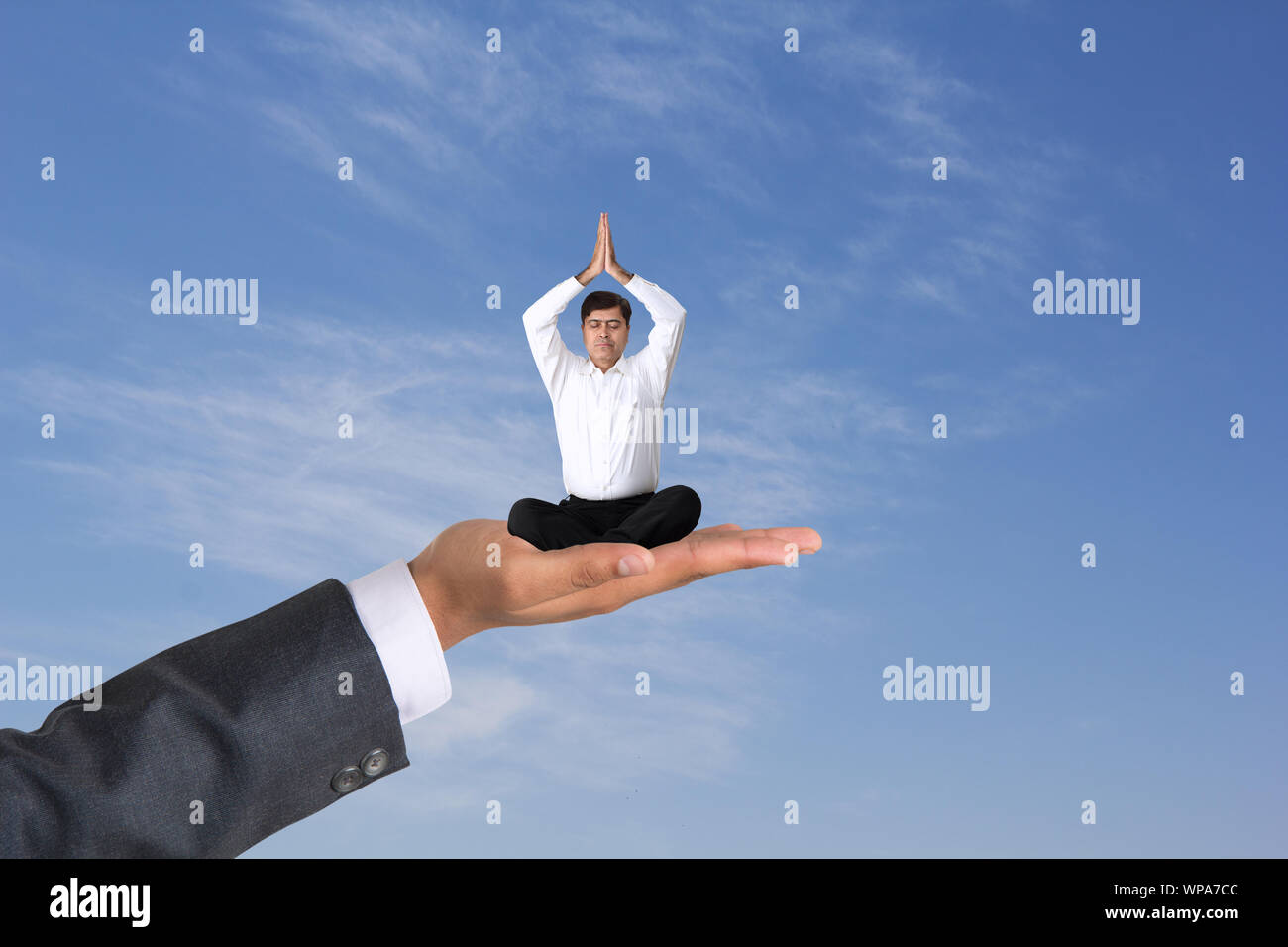 Uomo d'affari seduto su una mano umana e che fa yoga posa Foto Stock