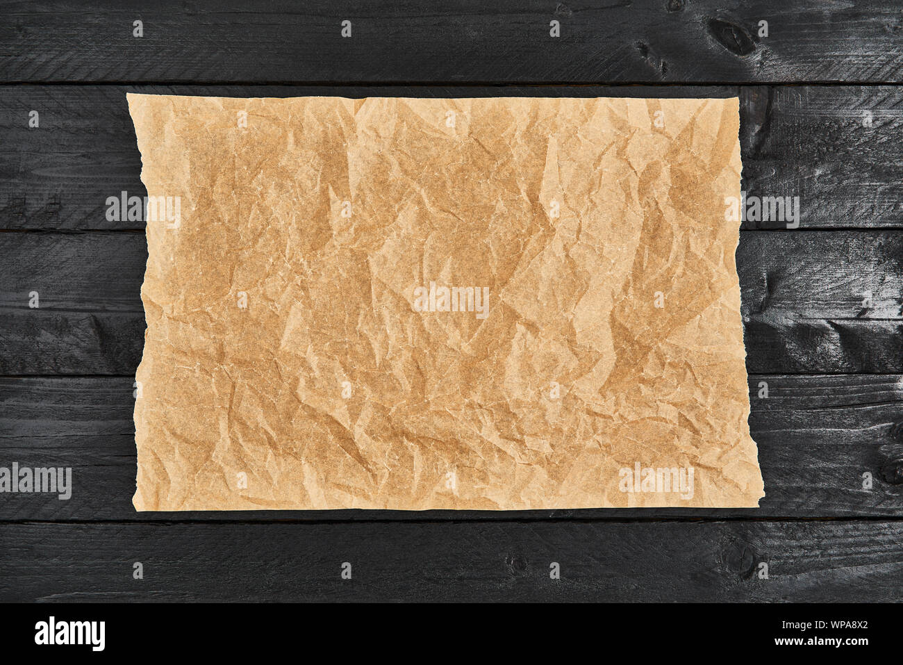 Crumpled pezzo di pergamena o carta da forno su tavoli in legno nero. Vista dall'alto. Copia spazio per testo e elemento di design. Foto Stock