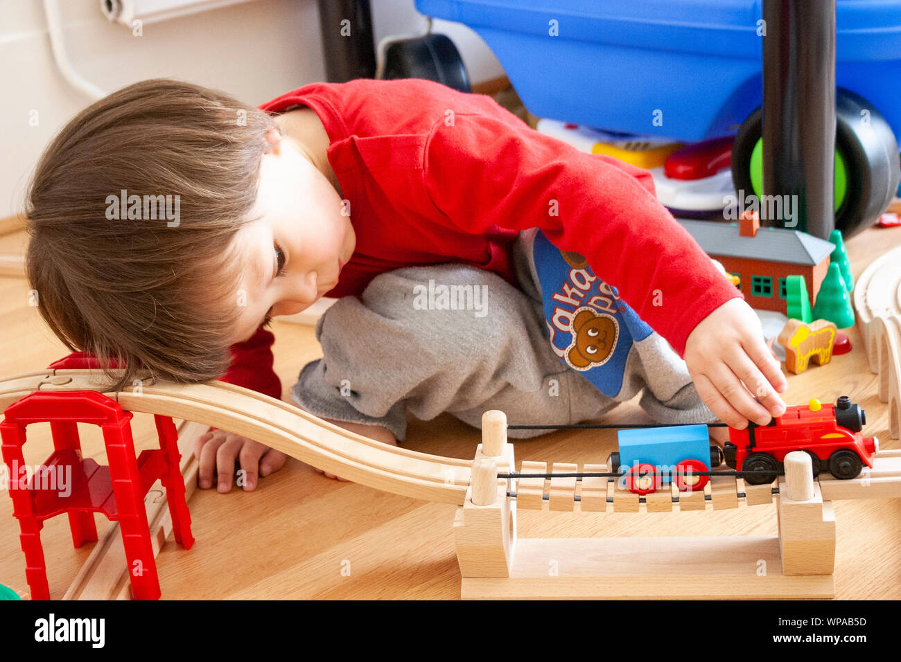 Bambino caucasico, 3-4 anni, all'interno. Il livello del pavimento vista del giovane ragazzo giocando con Thomas Tank Engine train set. Spingendo il treno lungo la via. Foto Stock