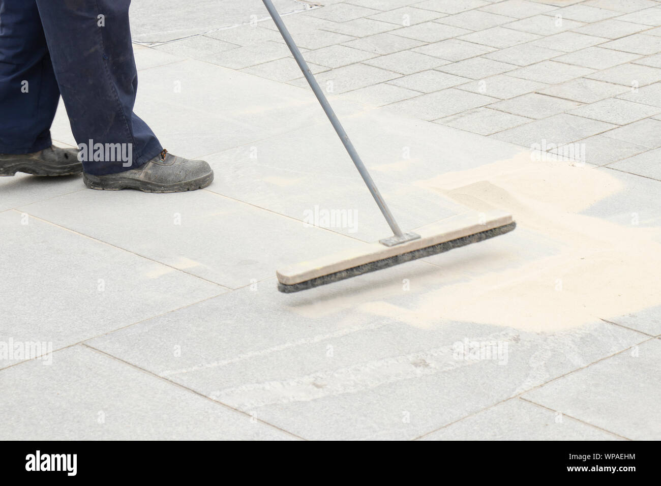Marciapiede lavoratore edile di riempimento del blocco giunti con sabbia utilizzando scopa lunga, finitura pavimentazione stradale Foto Stock