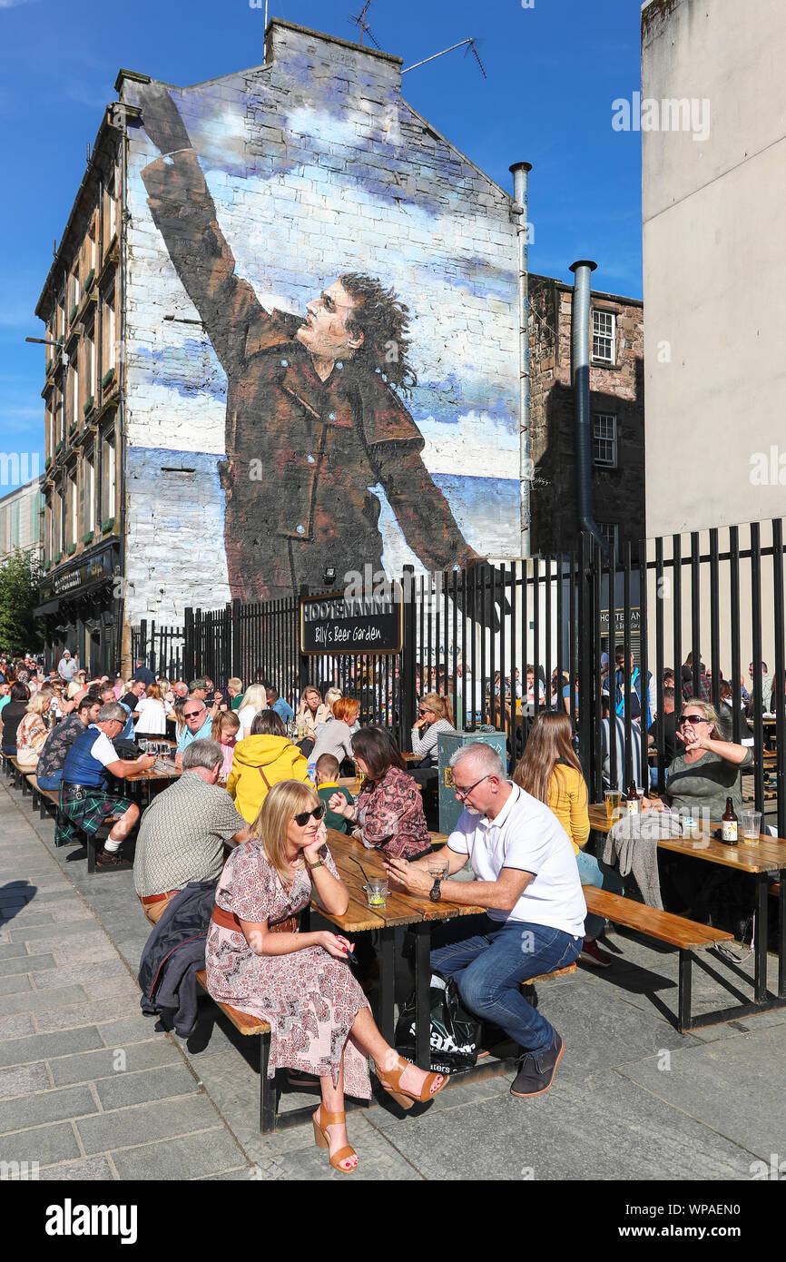Turisti che si siedono sui posti a sedere all'aperto presso il pub Hootenanny nella zona denominata Billy beer garden dopo la parete murale di Billy Connolly, il famoso Foto Stock