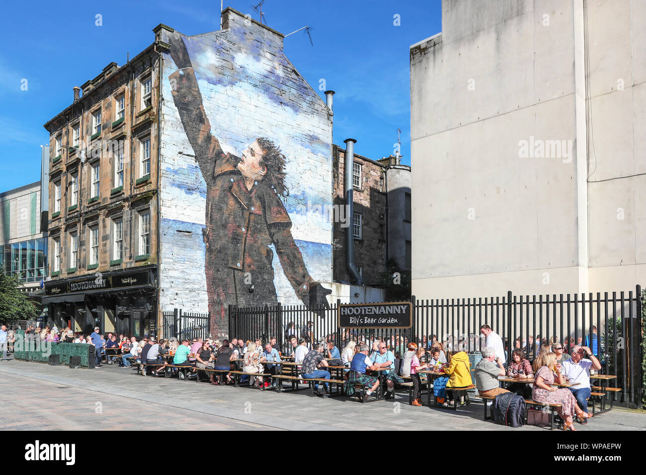 Turisti che si siedono sui posti a sedere all'aperto presso il pub Hootenanny nella zona denominata Billy beer garden dopo la parete murale di Billy Connolly, il famoso Foto Stock