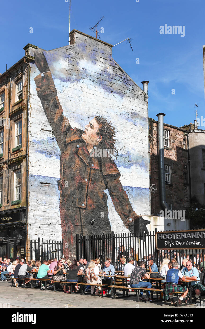 Turisti che si siedono sui posti a sedere all'aperto presso il pub Hootenanny nella zona denominata Billy beer garden dopo la parete murale di Billy Connolly, il famoso Foto Stock