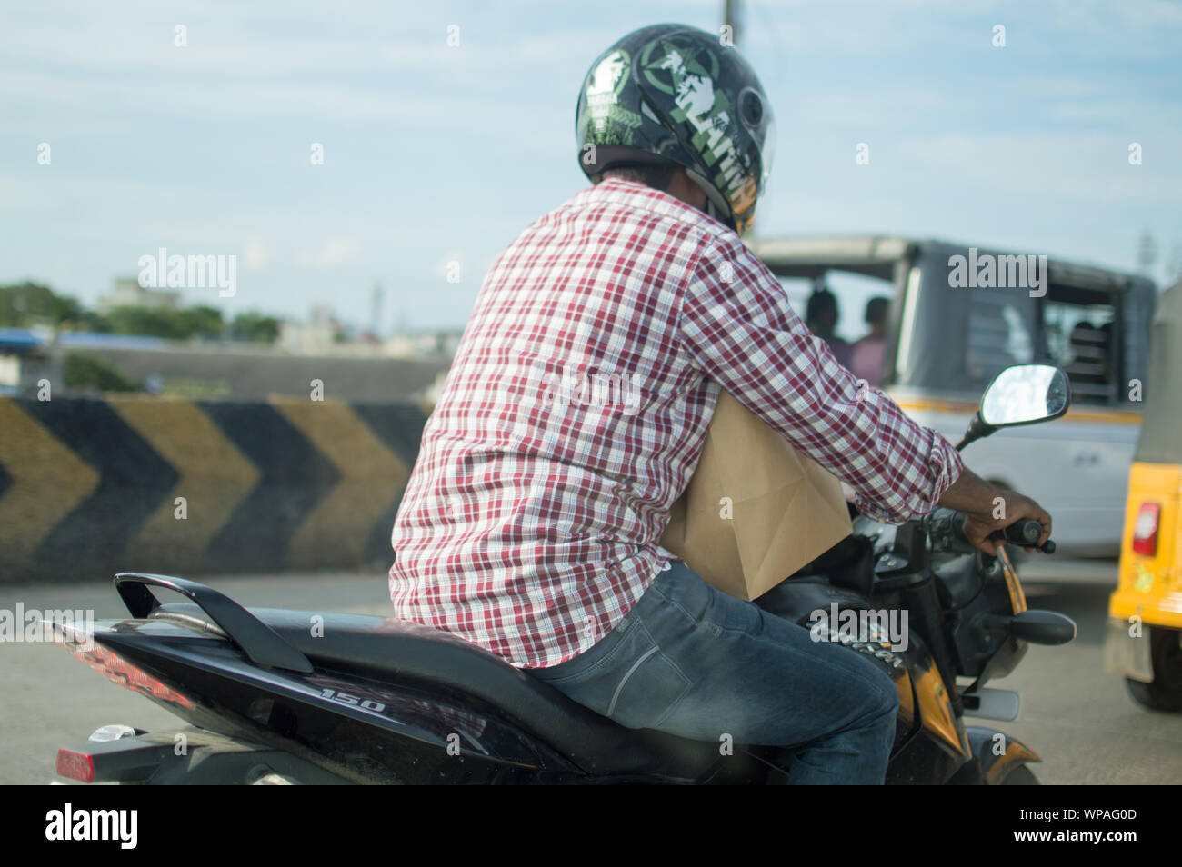 Un uomo con il casco su una bici attraverso le strade della città di Chennai / Madras Foto Stock