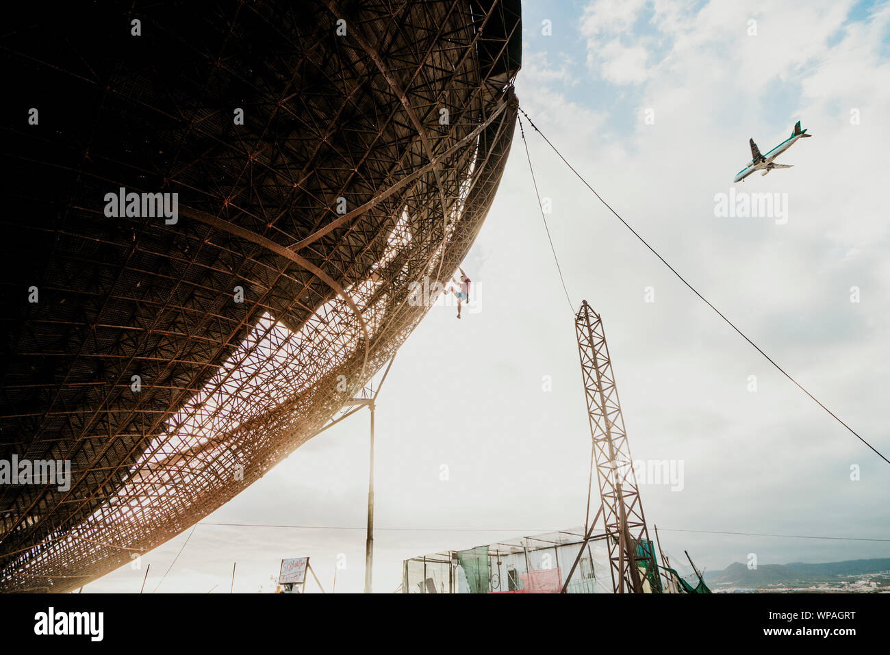 L'uomo scalata di un enorme parabola satellitare durante il tramonto vicino ad un aereo Foto Stock
