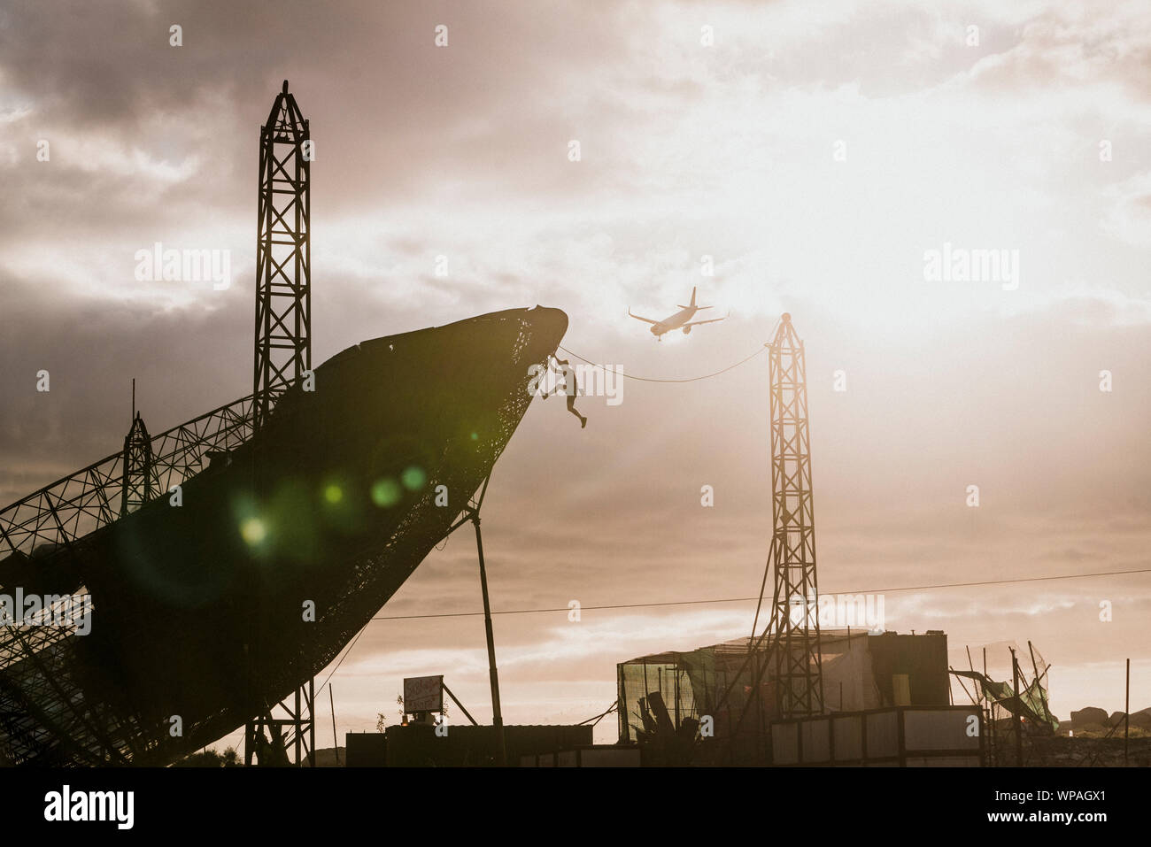 L'uomo scalata di un enorme parabola satellitare durante il tramonto Foto Stock