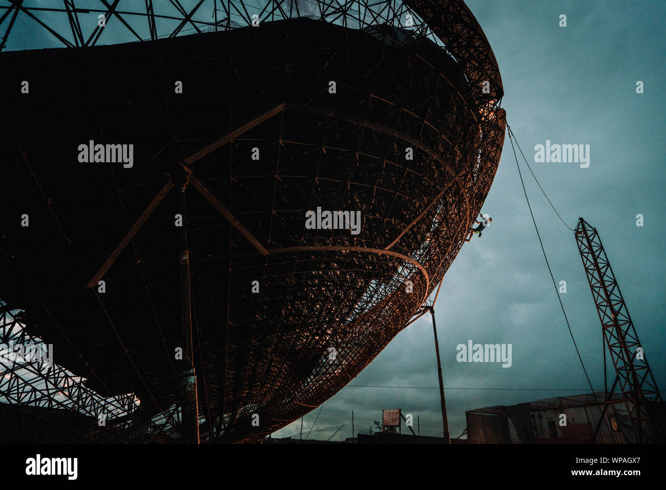 L'uomo scalata di un enorme parabola satellitare durante ore blu Foto Stock