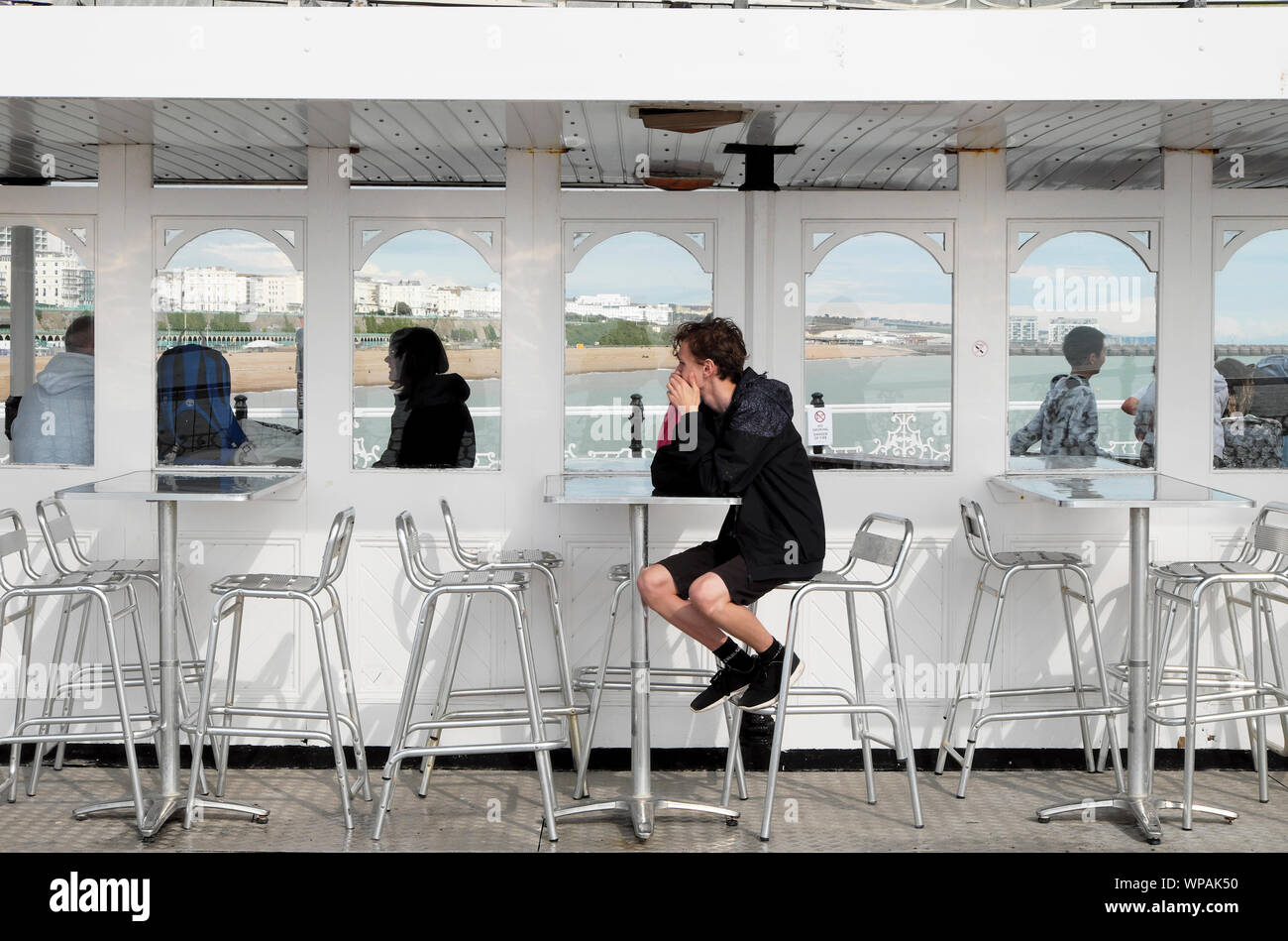 Giovane uomo seduto da solo a un tavolo in un giorno di pioggia sul molo di Brighton in East Sussex England Regno Unito KATHY DEWITT Foto Stock