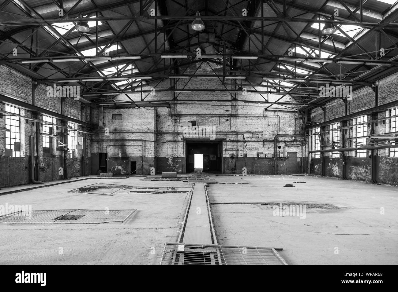 Tono di BW,vista interna del vuoto piano aperto di abbandonare la ex fabbrica di officina con danni di elementi di costruzione, a parete, windows e soffitti con nessuno. Foto Stock