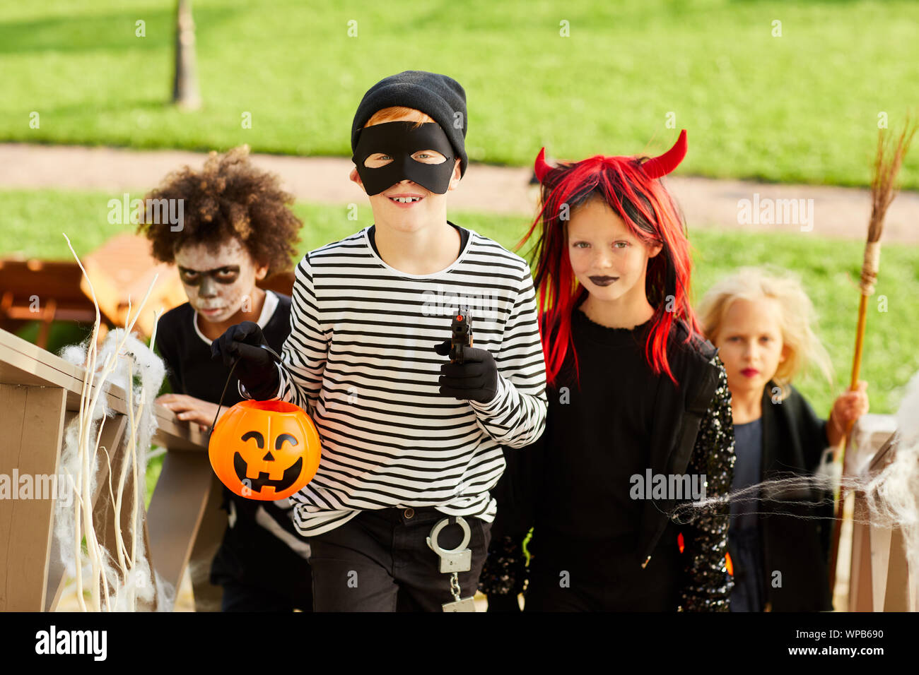 Multi-etnico gruppo di bambini trucco o trattare su Halloween in piedi sulle scale in fila, concentrarsi sul ragazzo sorridente indossando il costume e tenendo la zucca paniere Foto Stock