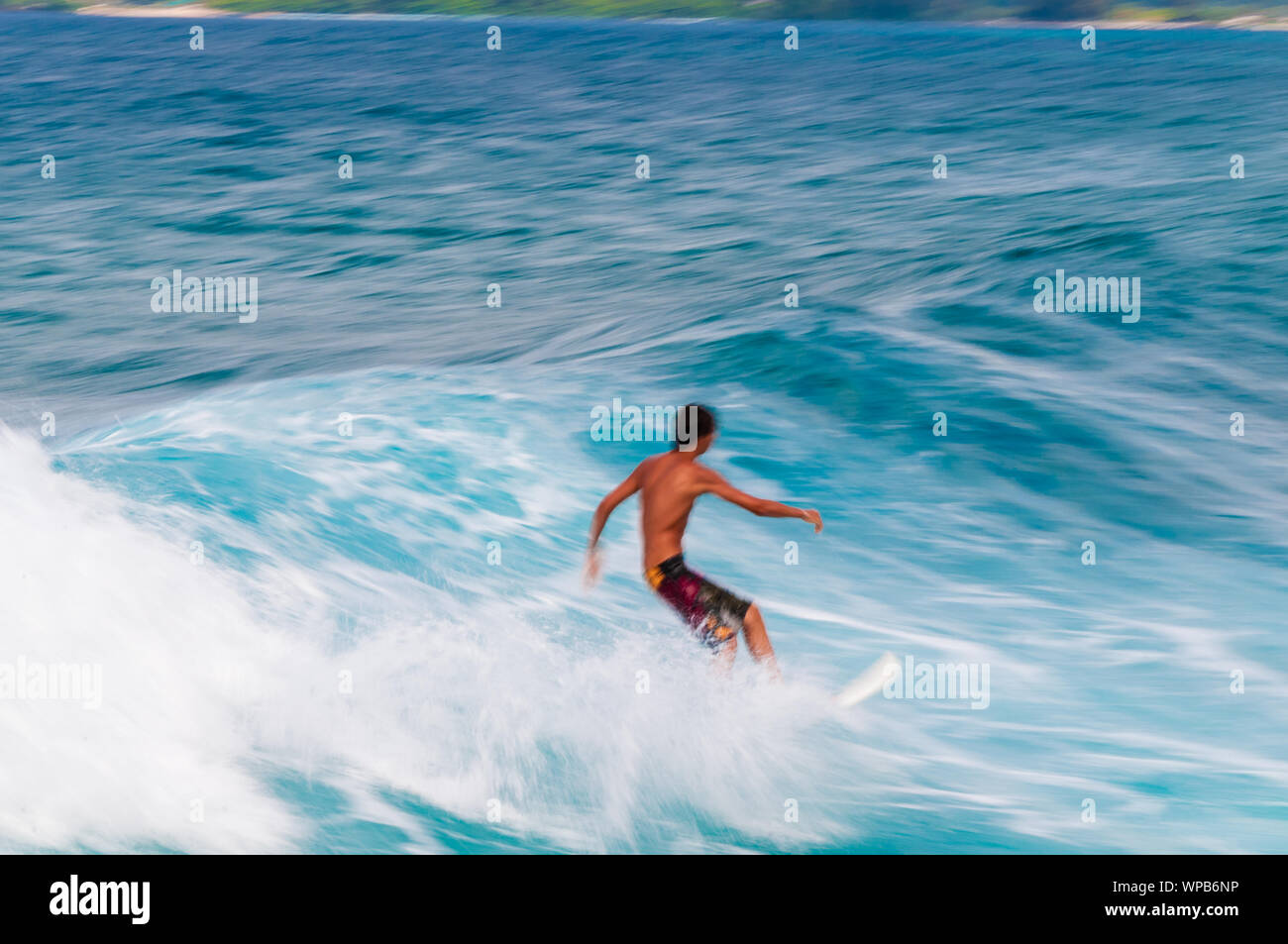 Giovane uomo che cavalca una tavola da surf in una onda blu in estate. Foto Stock