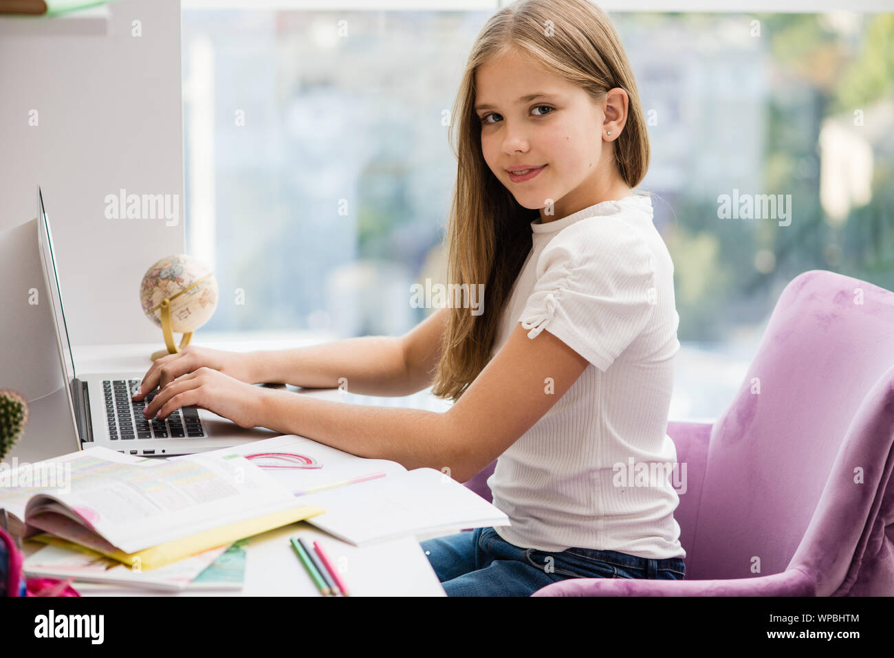 Bella ragazza scuola seduti alla scrivania con computer portatile in una buona postura. Home interni. Foto Stock