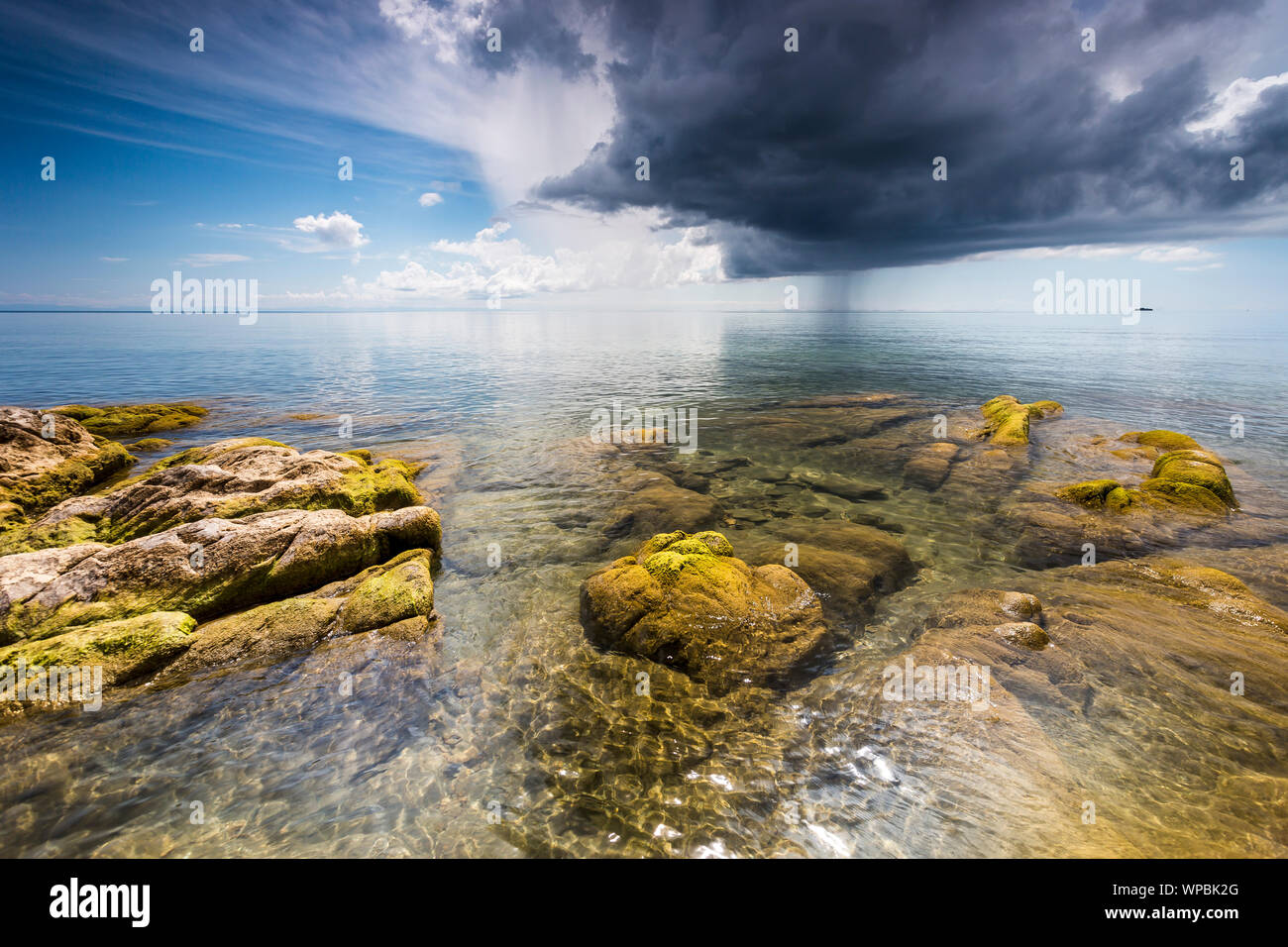 Acqua cristallina verde con pietre di muschio presso il Lago Malawi, Dark nuvole temporalesche nel cielo, Africa Foto Stock