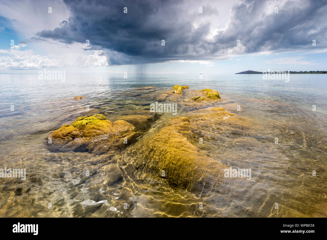 Acqua cristallina verde con pietre di muschio presso il Lago Malawi, Dark nuvole temporalesche nel cielo, Africa Foto Stock