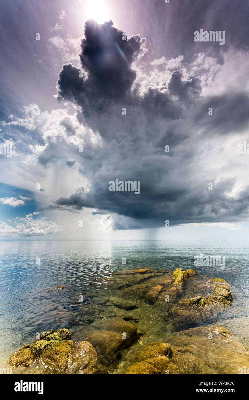 Acqua cristallina verde con pietre di muschio presso il Lago Malawi, Dark nuvole temporalesche nel cielo, Africa Foto Stock
