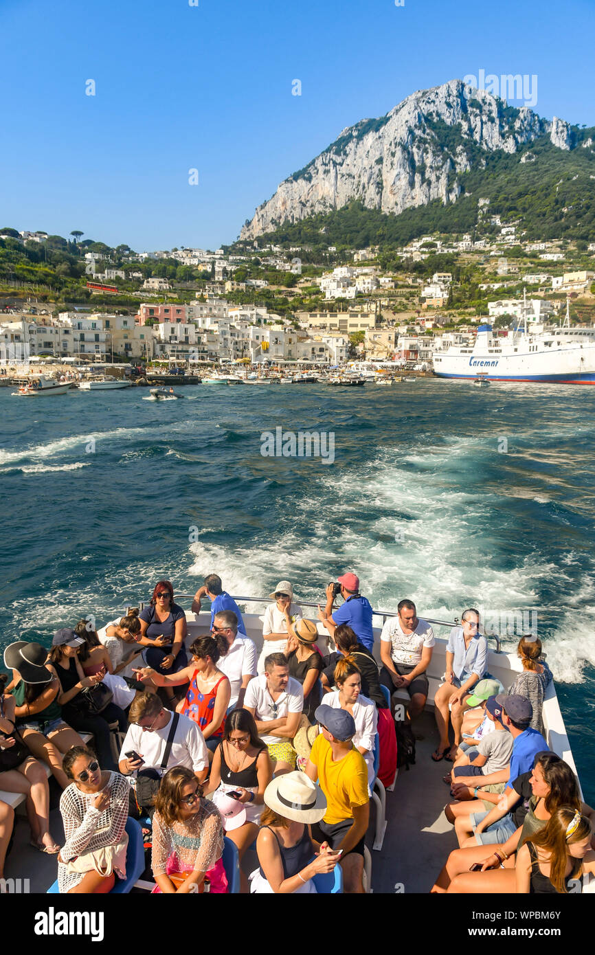 Isola di Capri - Agosto 2019: i passeggeri a bordo di una barca di lasciare il porto dell'isola di Capri. Un traghetto è ormeggiata nel porto. Foto Stock
