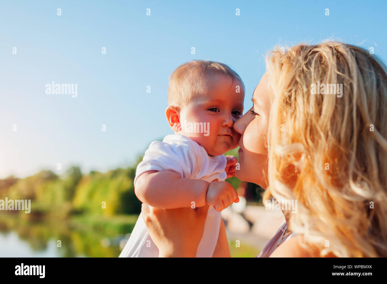 Giovane madre holding baby vicino al suo volto. Famiglia passeggiate nel parco al tramonto Foto Stock