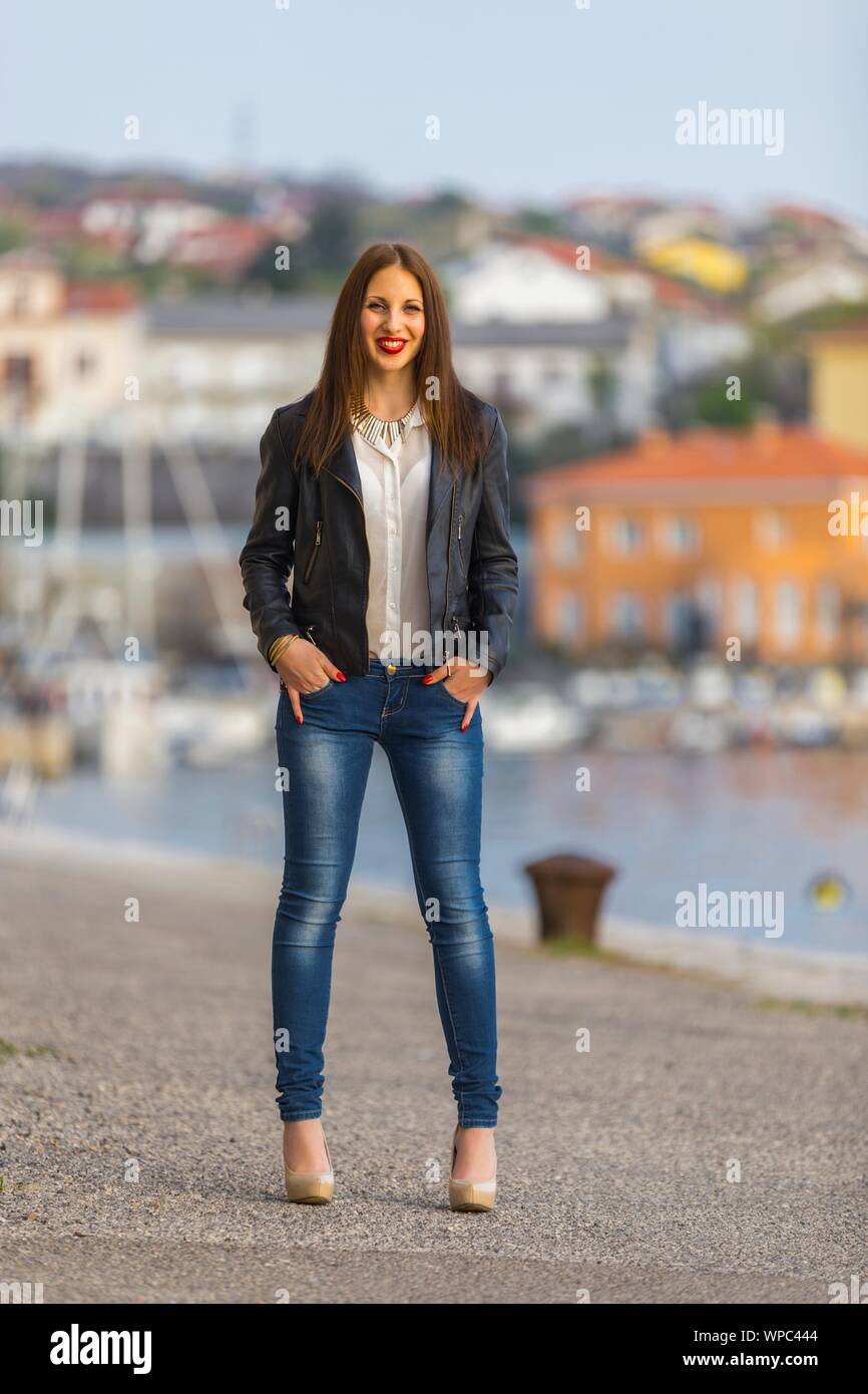 Teen girl in denim pantaloni Beige high-heels in piedi sul mare mani dita in tasche guardando la fotocamera occhio occhi-contatto occhi eyeshot Sorridente Red-Lips Foto Stock