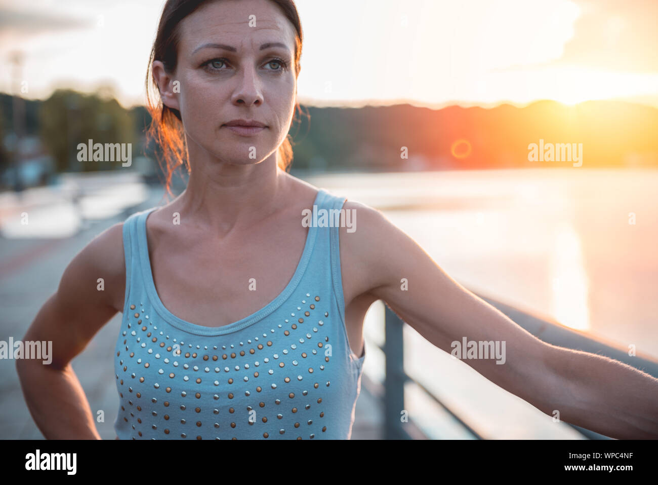 Triste donna in piedi dall'acqua durante il tramonto Foto Stock