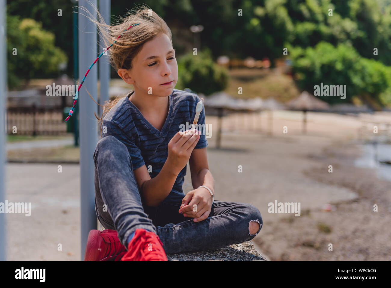 Ragazza seduta su un terrapieno e mangiare il gelato Foto Stock