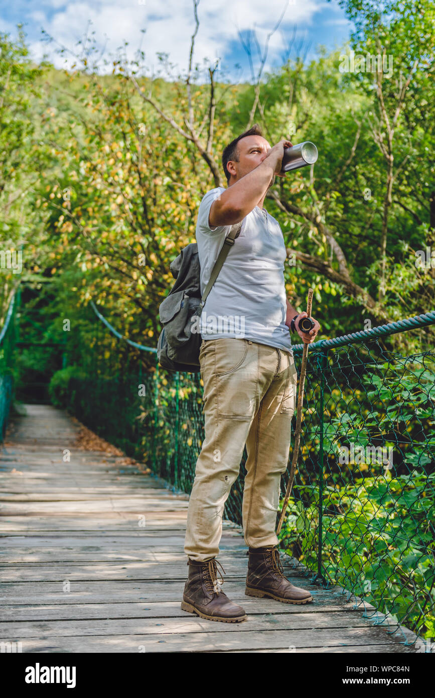 Escursionista in piedi sul legno ponte di sospensione nella foresta e acqua potabile Foto Stock