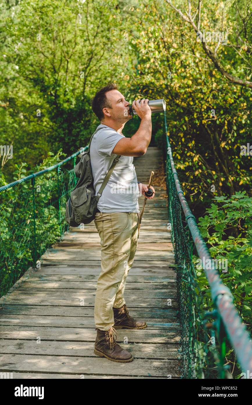 Escursionista in piedi sul legno ponte di sospensione nella foresta e acqua potabile Foto Stock Escursionista in piedi sul legno ponte di sospensione nella foresta e acqua potabile Foto Stock