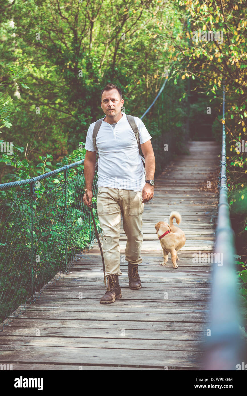 Escursionista con small yellow dog camminare su legno ponte di sospensione nella foresta Foto Stock