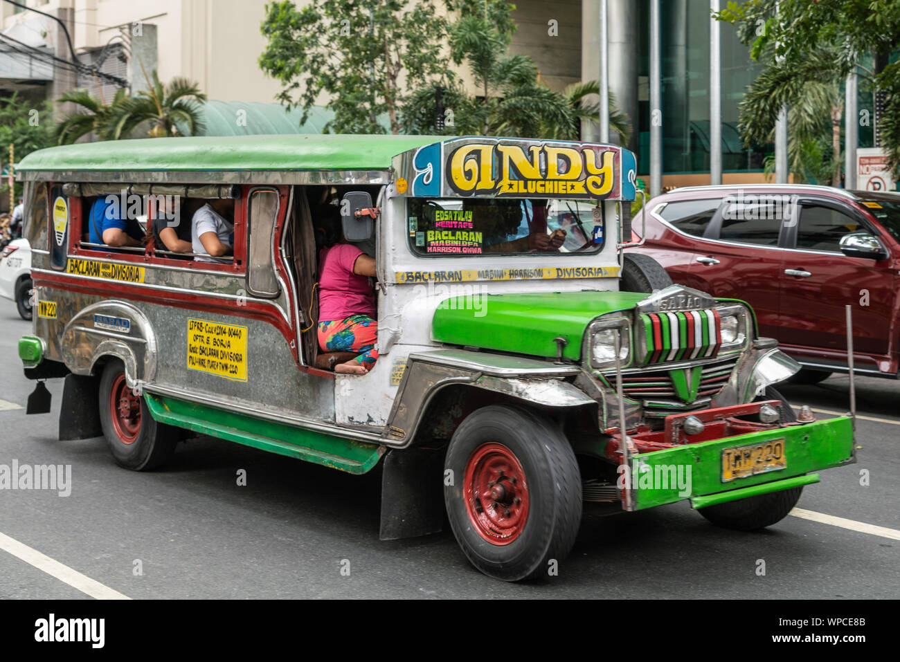 Manila, Filippine - Marzo 5, 2019: verde e grigio Jeep lungo il trasporto pubblico in strada. Vista laterale e frontale. Le persone all'interno. Il verde delle foglie. Altre Auto Foto Stock