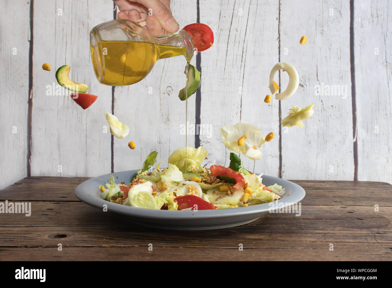 Mano umana versando olio d'oliva per l'insalata di volare intorno. Fotografia fantasia Foto Stock