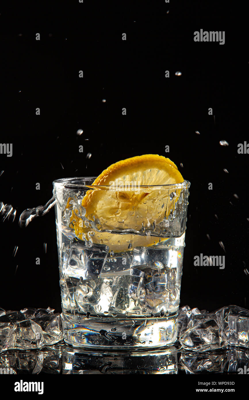 Bicchiere di acqua, i cristalli di ghiaccio e limone su un nero di sfondo per studio Foto Stock