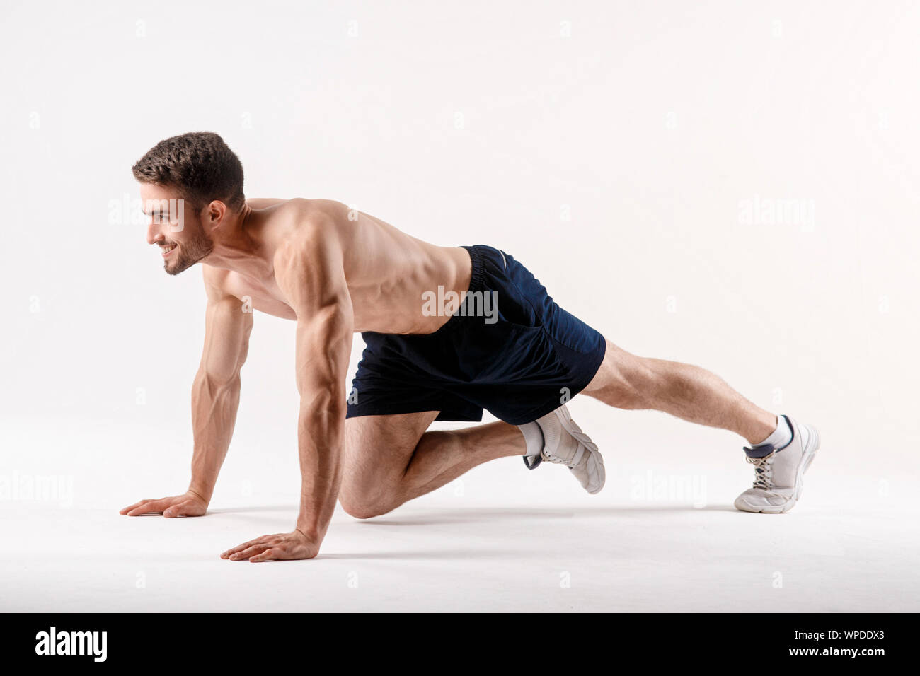 Giovane uomo con una barba di una corporatura sportiva fa un esercizio sui muscoli della cavità addominale su un bianco sfondo isolato, l'atleta va in per lo sport, Foto Stock