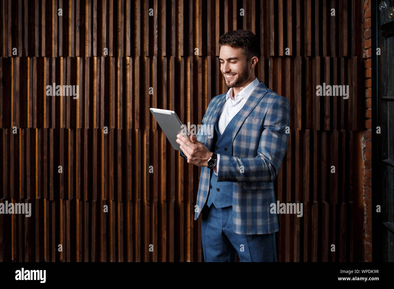 Giovane imprenditore di successo con la barba in un lussuoso blu tuta controllati. L'uomo lavora su un tablet in un loft ufficio. Foto Stock