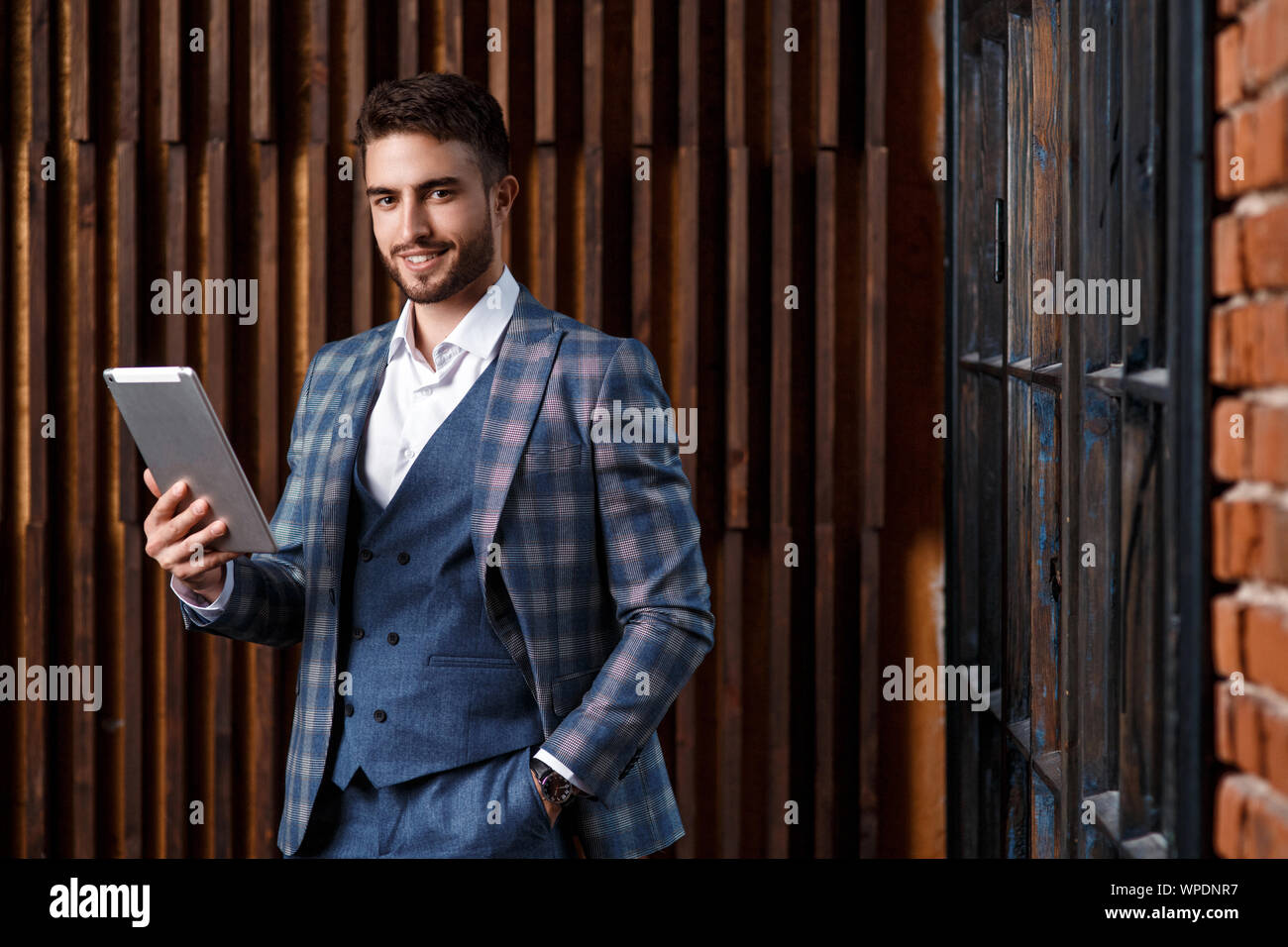 Giovane imprenditore di successo con la barba in un lussuoso blu tuta controllati. L'uomo lavora su un tablet in un loft ufficio. Foto Stock