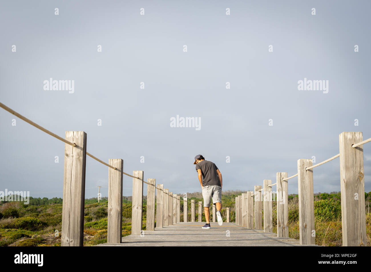 Un uomo che indossa un cappello per il sole, vista dal retro in una distanza, guardando verso il basso con un solo piede su una passerella di legno. Circondato dalla natura. Foto Stock