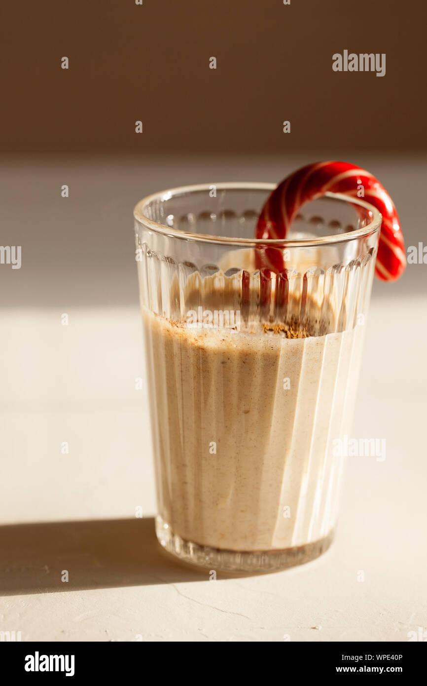 Tradizionale winter in casa gustosi cocktail di Natale zabaione con latte,rum, cannella e noce moscata decorate candy cane su sfondo bianco con ombra Foto Stock