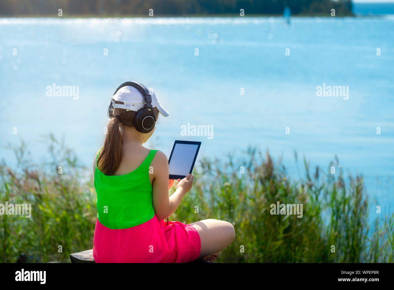 Ragazza giovane è la lettura di ebook sul banco vicino al mare, anche lei sta godendo del caldo giorno d'estate Foto Stock