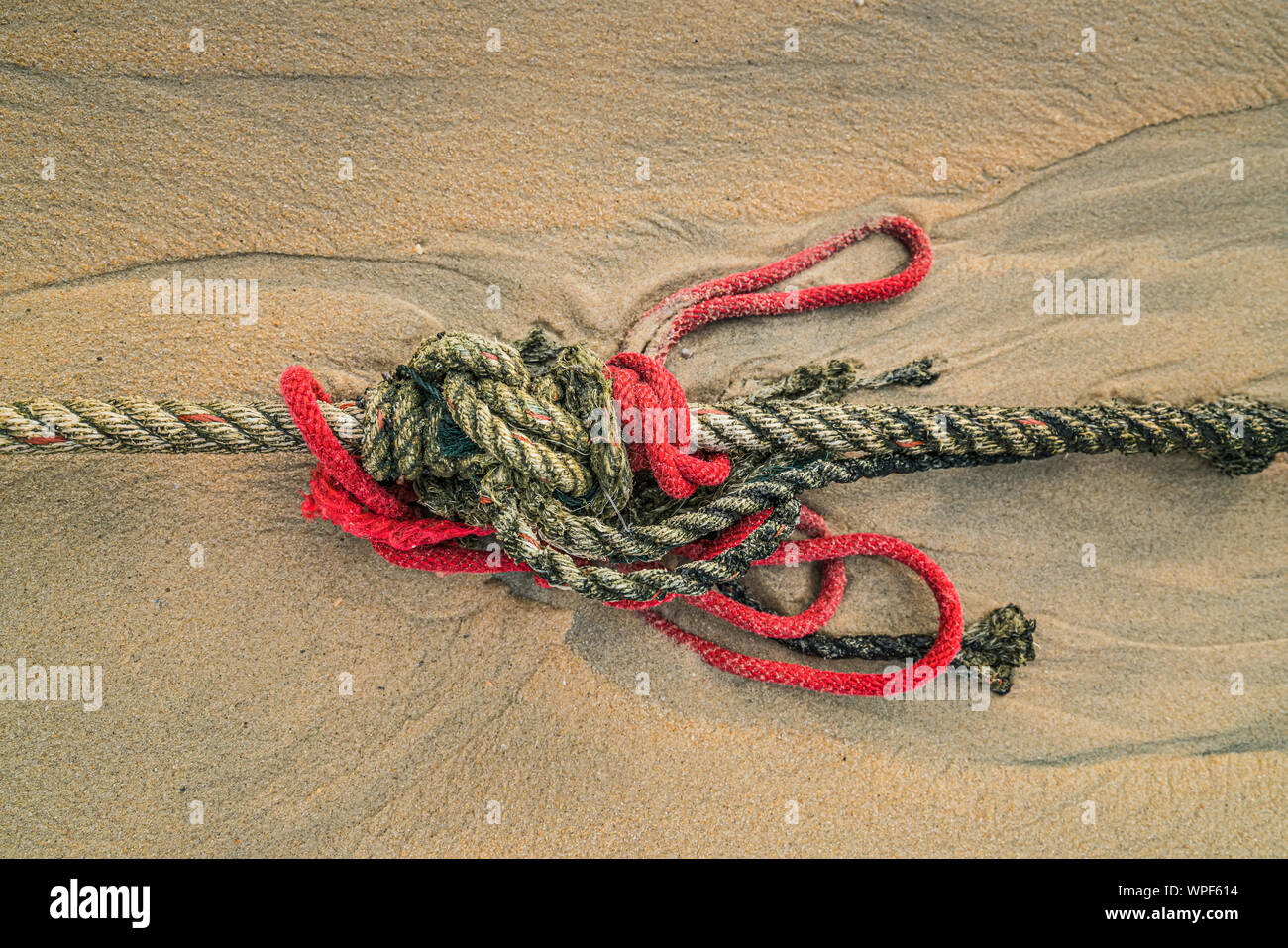 Creative rosso navi annodato la corda che giace su di una spiaggia di sabbia che conduce al mare sulla costa come la marea arriva a. Foto Stock