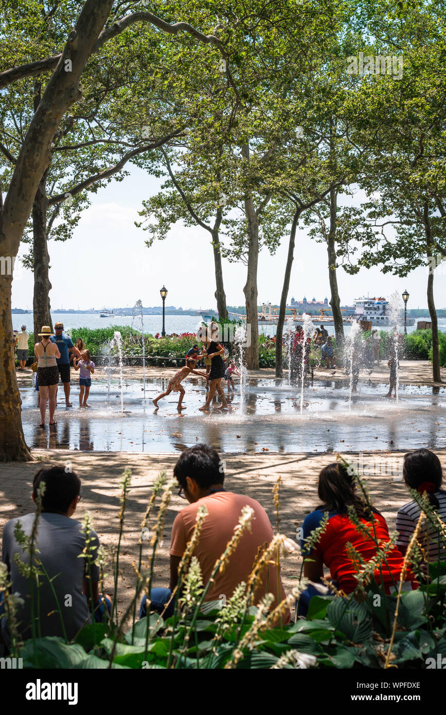 Battery Park New York, vista in estate di persone godendo il getto d'acqua in funzione Battery Park, la parte inferiore di Manhattan, New York City, Stati Uniti d'America Foto Stock