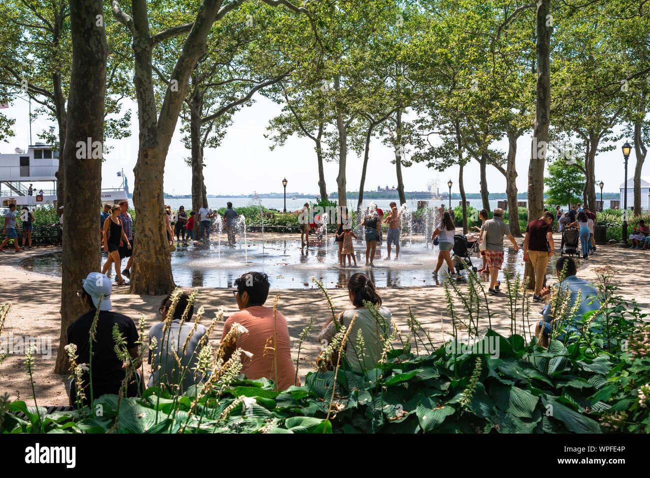Battery Park New York, vista in estate di persone godendo il getto d'acqua in funzione Battery Park, la parte inferiore di Manhattan, New York City, Stati Uniti d'America Foto Stock
