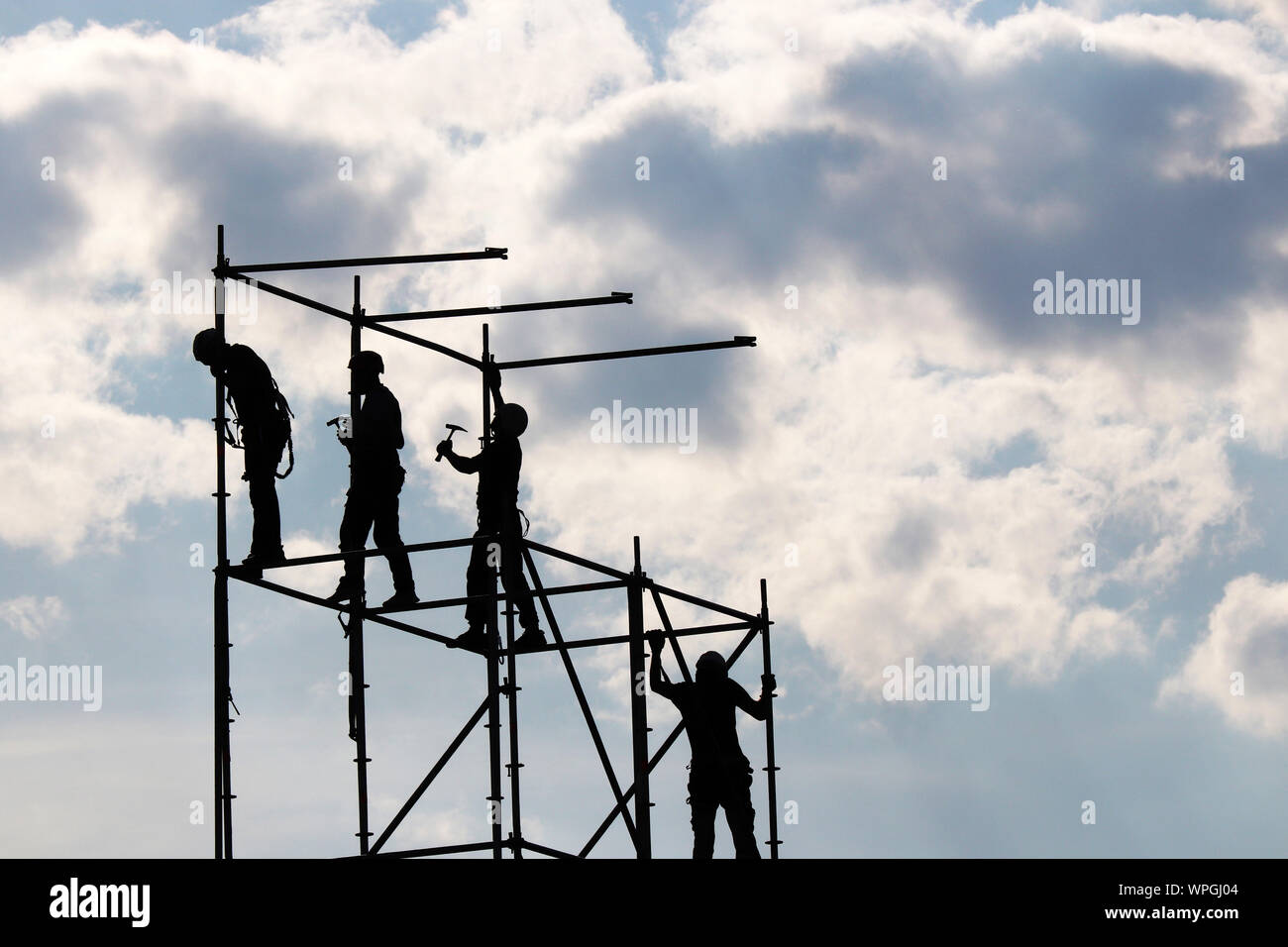 Lavoratori edili di ponteggi. Sagome di persone che lavorano sul sito di costruzione contro il cielo blu con nuvole bianche Foto Stock