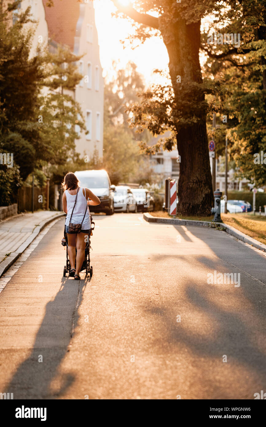 Vista posteriore di una madre spingere un passeggino sul eveining di una soleggiata giornata estiva in un bellissimo paesaggio urbano Foto Stock
