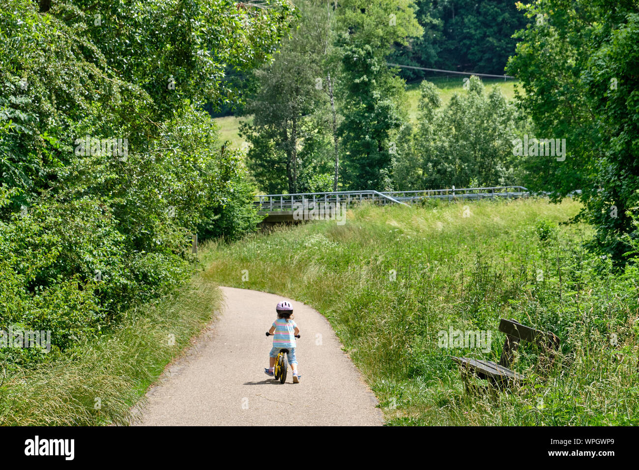 Vista posteriore di un bambino sul suo equilibrio bicicletta su un percorso di ciclo in un idilliaco paesaggio verde paesaggio estivo Foto Stock
