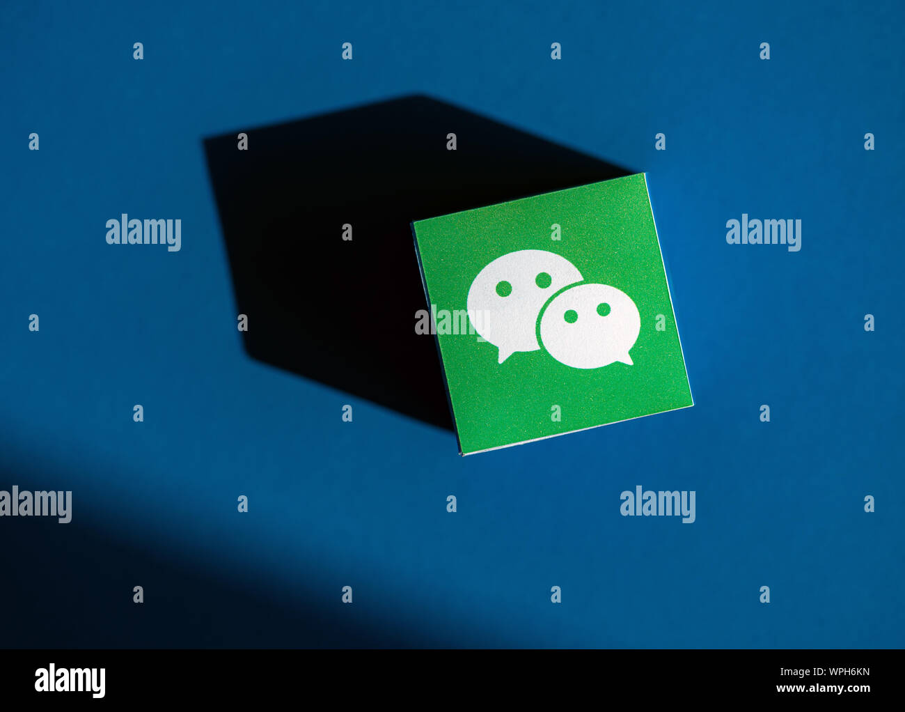 Un colpo dal di sopra del cubo di carta con il logo stampato dell'applicazione WeChat, che posto su uno sfondo blu. Foto Stock