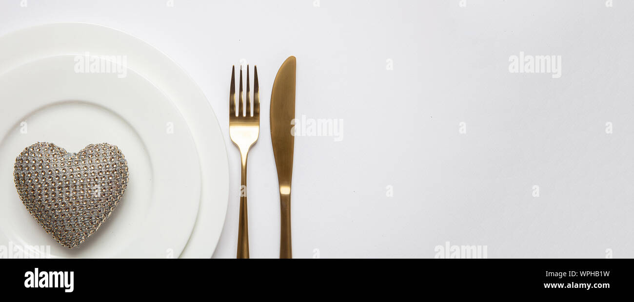 Anniversario di matrimonio la cena. Impostazione tabella oro e bianco, golden forchetta e coltello sul set di piatti, sfondo bianco, vista dall'alto Foto Stock