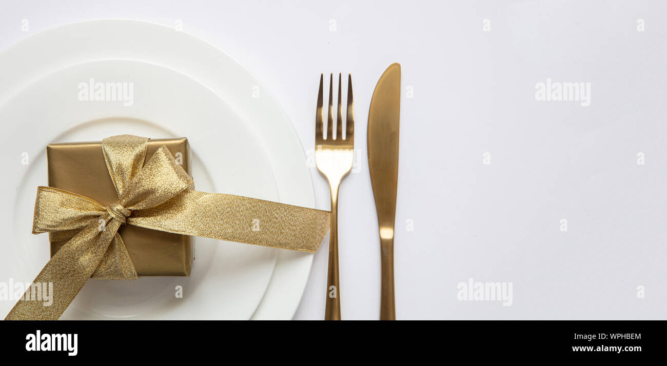 Cena di gala impostazione tabella, Gold confezione regalo e posate sul set di bianco di piatti, sfondo bianco, vista dall'alto, banner, spazio copto Foto Stock