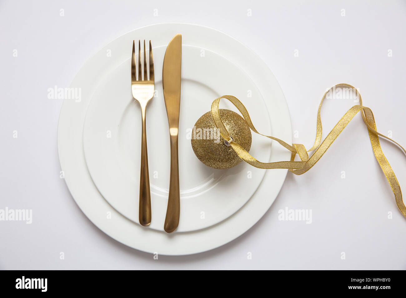 Il cenone di capodanno messa in tavola, oro xmas sfera con nastro e posate sul set di bianco di piatti, sfondo bianco, vista dall'alto Foto Stock